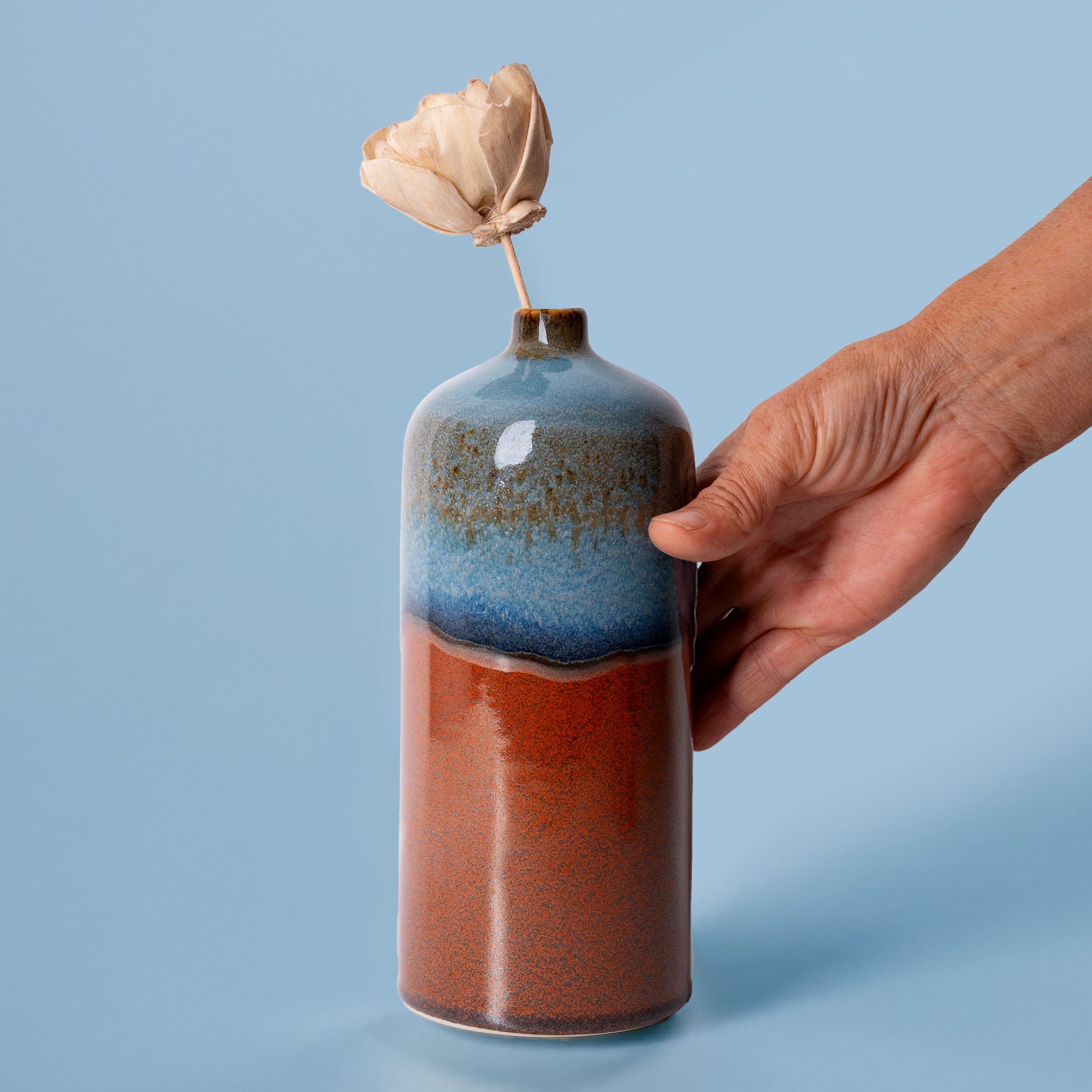 Pottery For The Planet medium decorative bud vase with blue and brown glaze held by a hand with dried flower