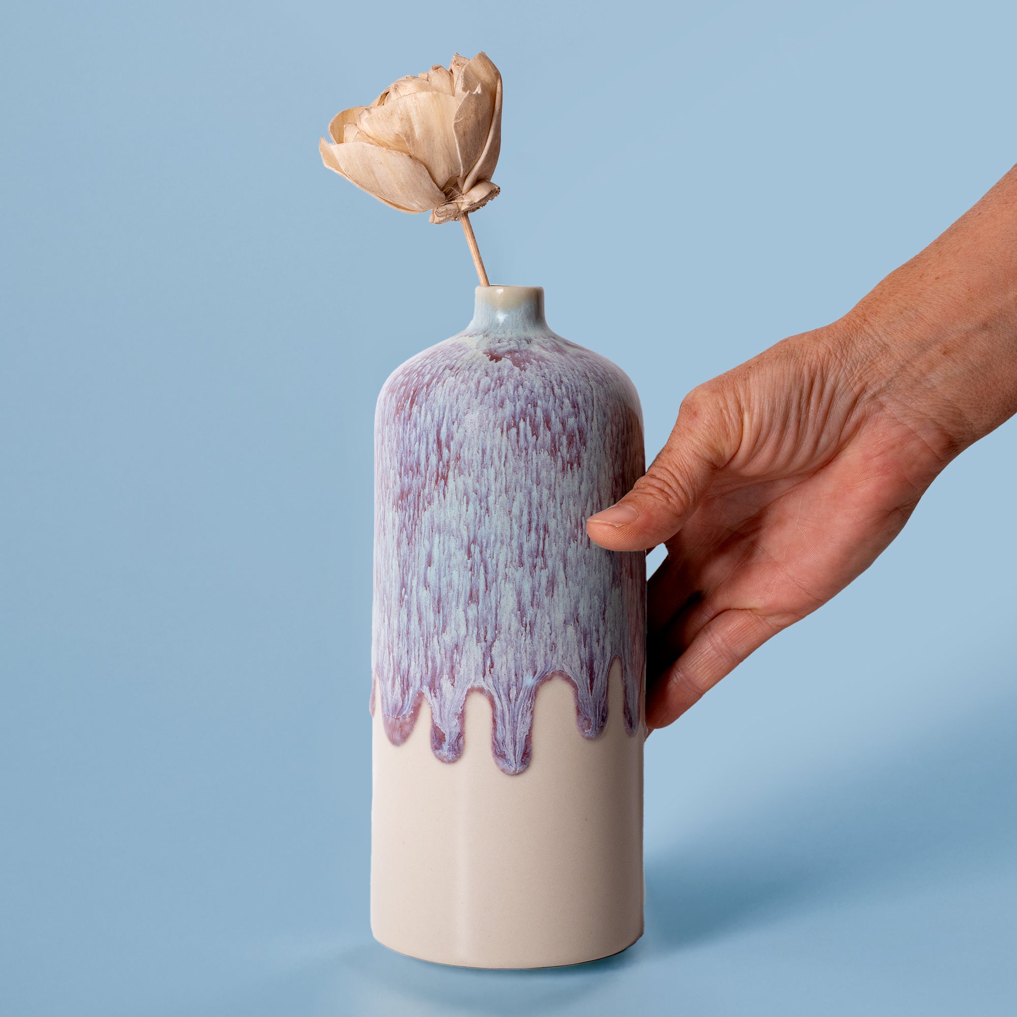 Pottery For The Planet medium decorative bud vase with purple glaze held by hand on blue background