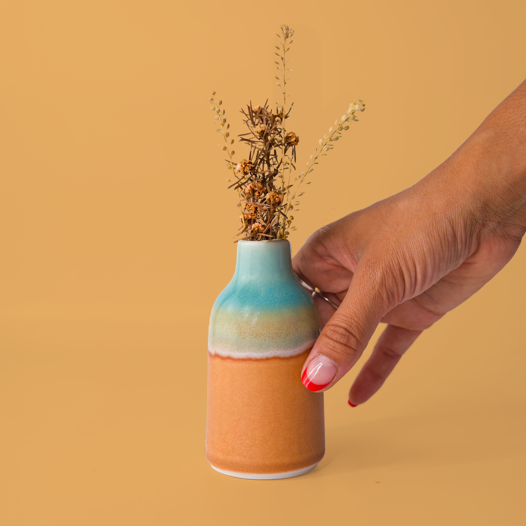 Hand holding modern decorative flower vase with blue and orange glaze and dried flowers