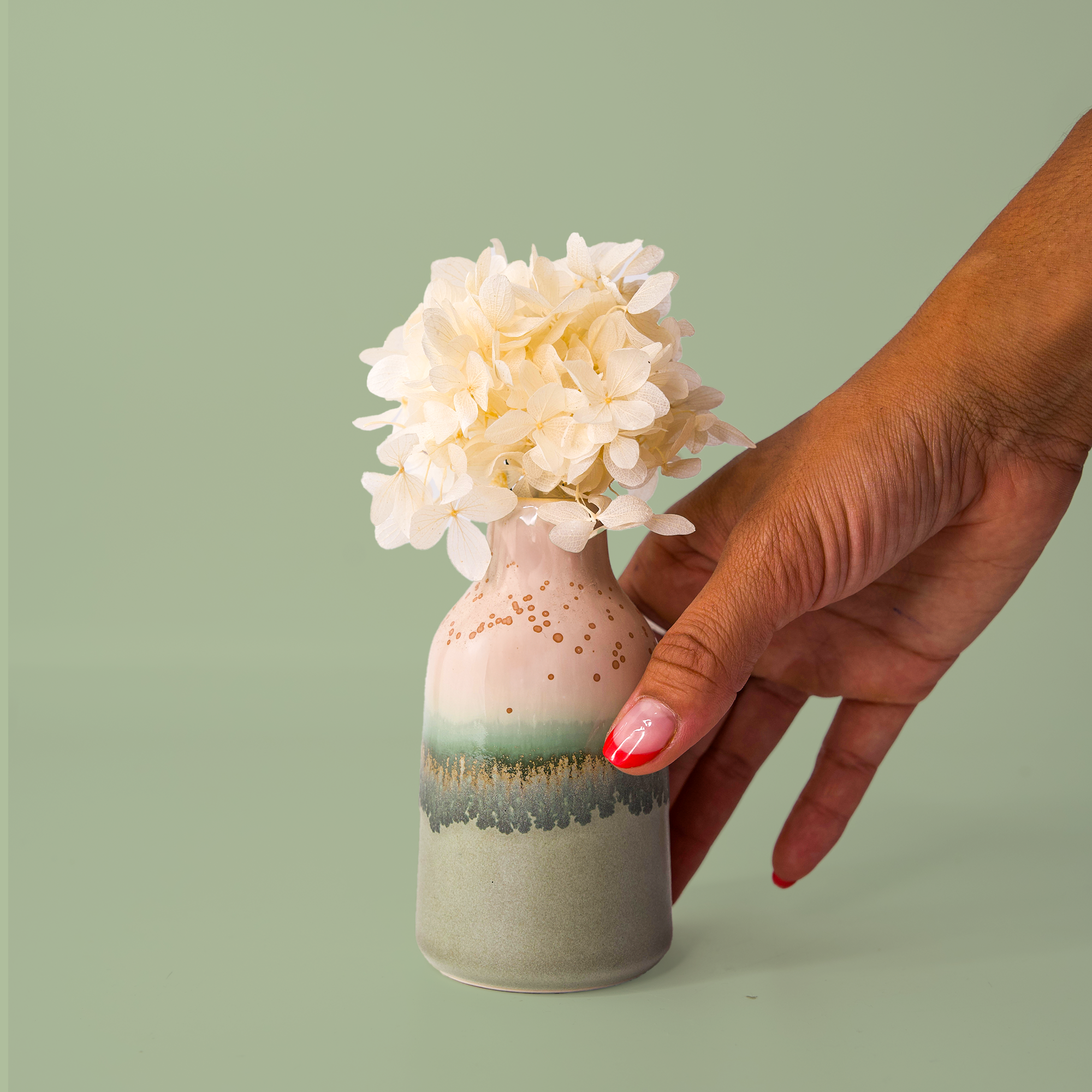 Hand holding modern decorative flower vase with gradient green and beige glaze and cream flowers