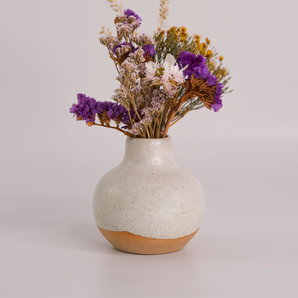 Small handmade home decor vase with a rounded shape holding dried purple and yellow flowers