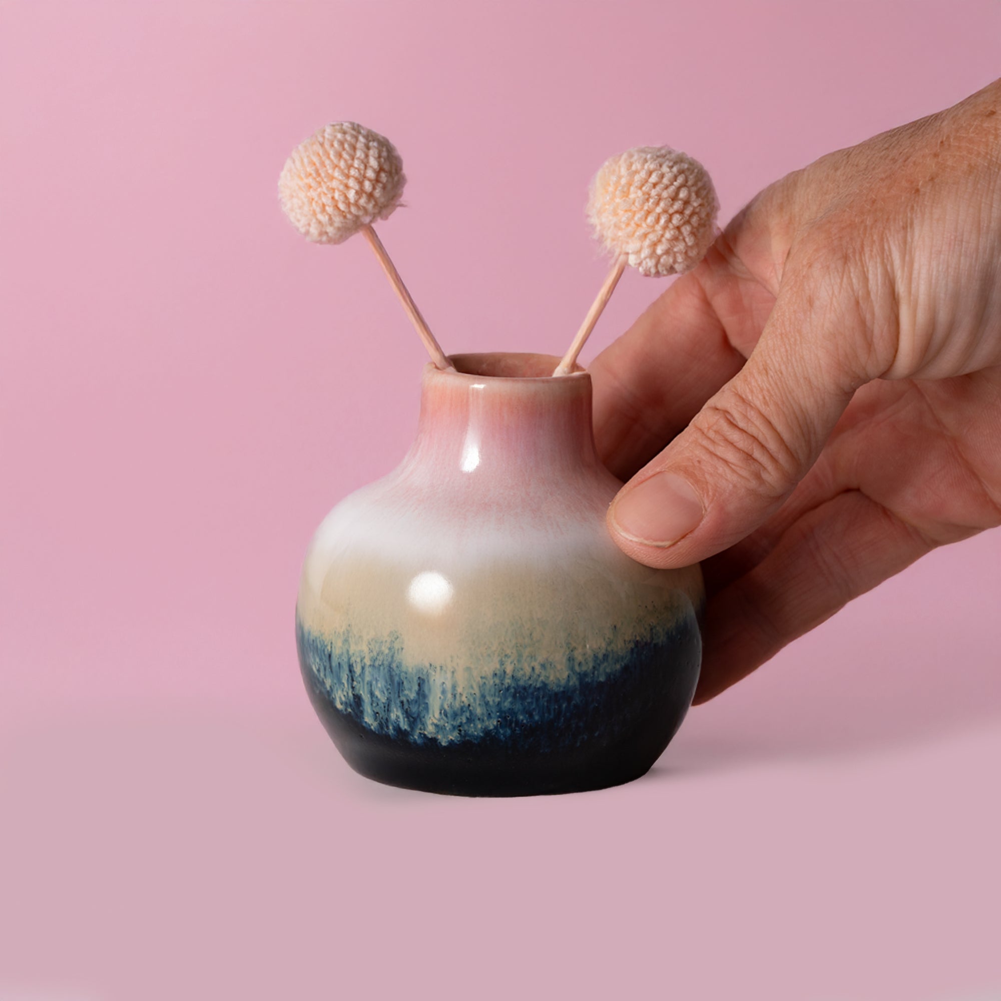 Small handmade home decor vase with pink, beige, and blue glaze held by hand with dried flowers