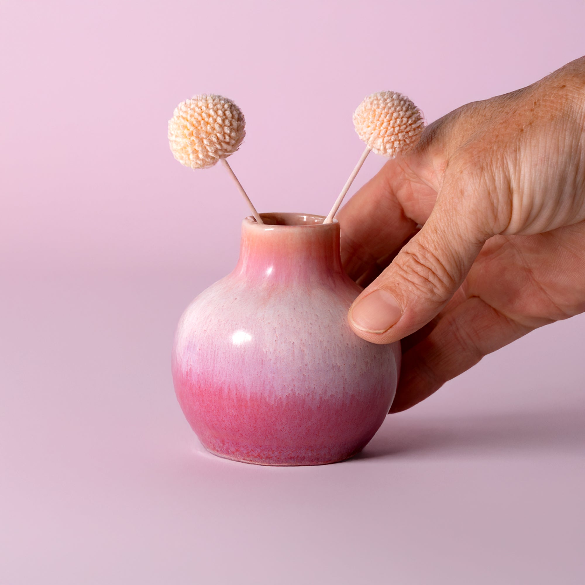 Small handmade home decor vase in pink gradient held by hand with two dried flowers inside