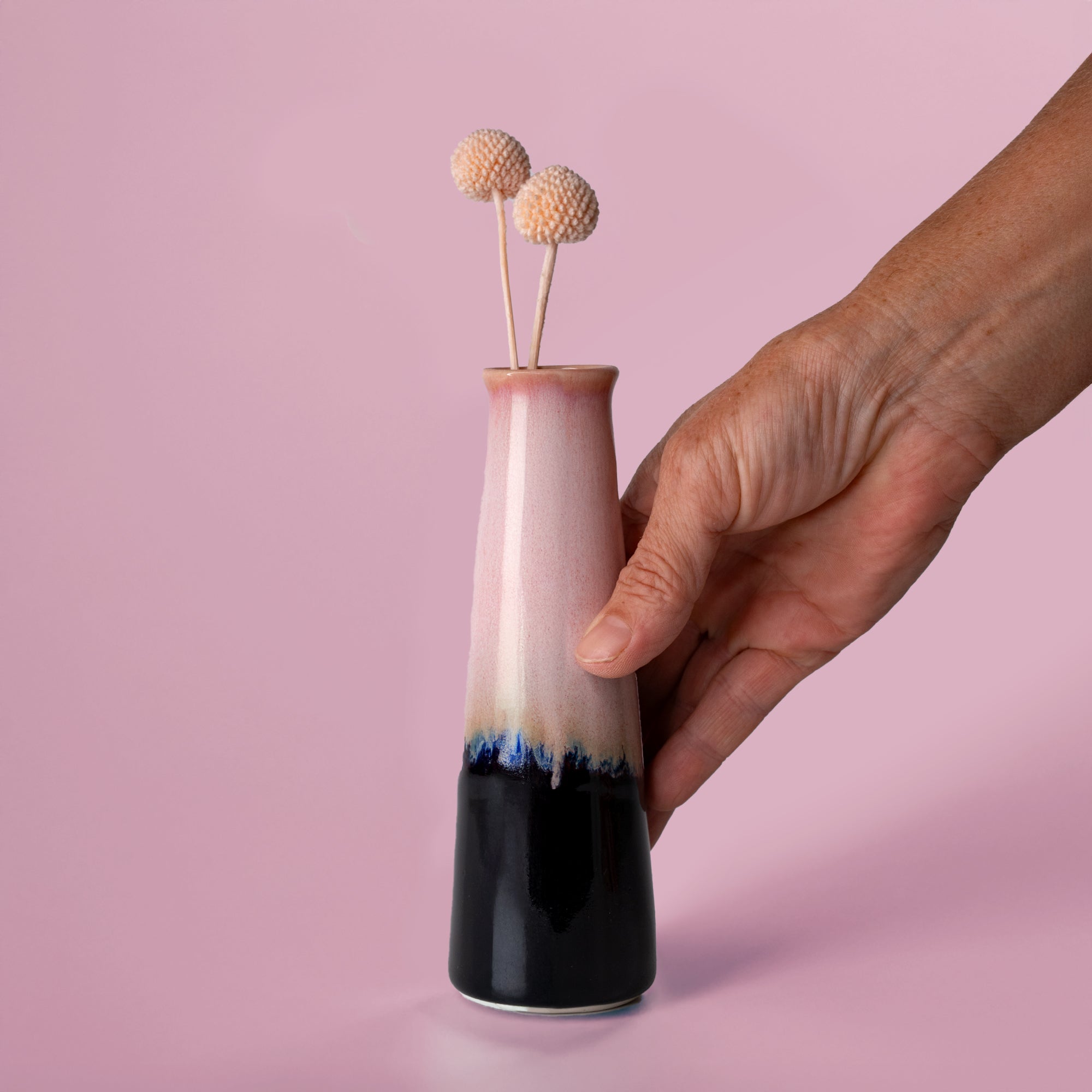 Hand holding a pink and black sustainable home decor vase with two dried flowers inside