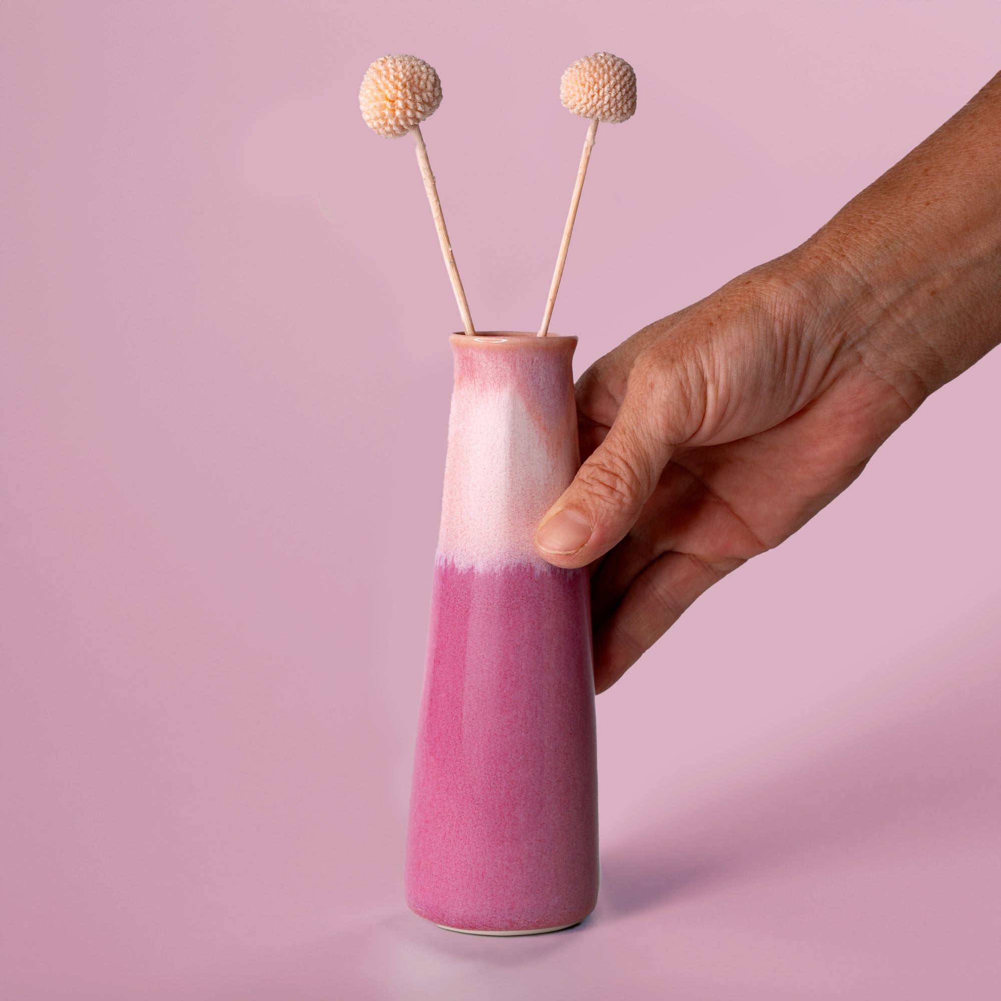 Hand holding a pink and white sustainable home decor vase from Pottery For The Planet with dried flowers