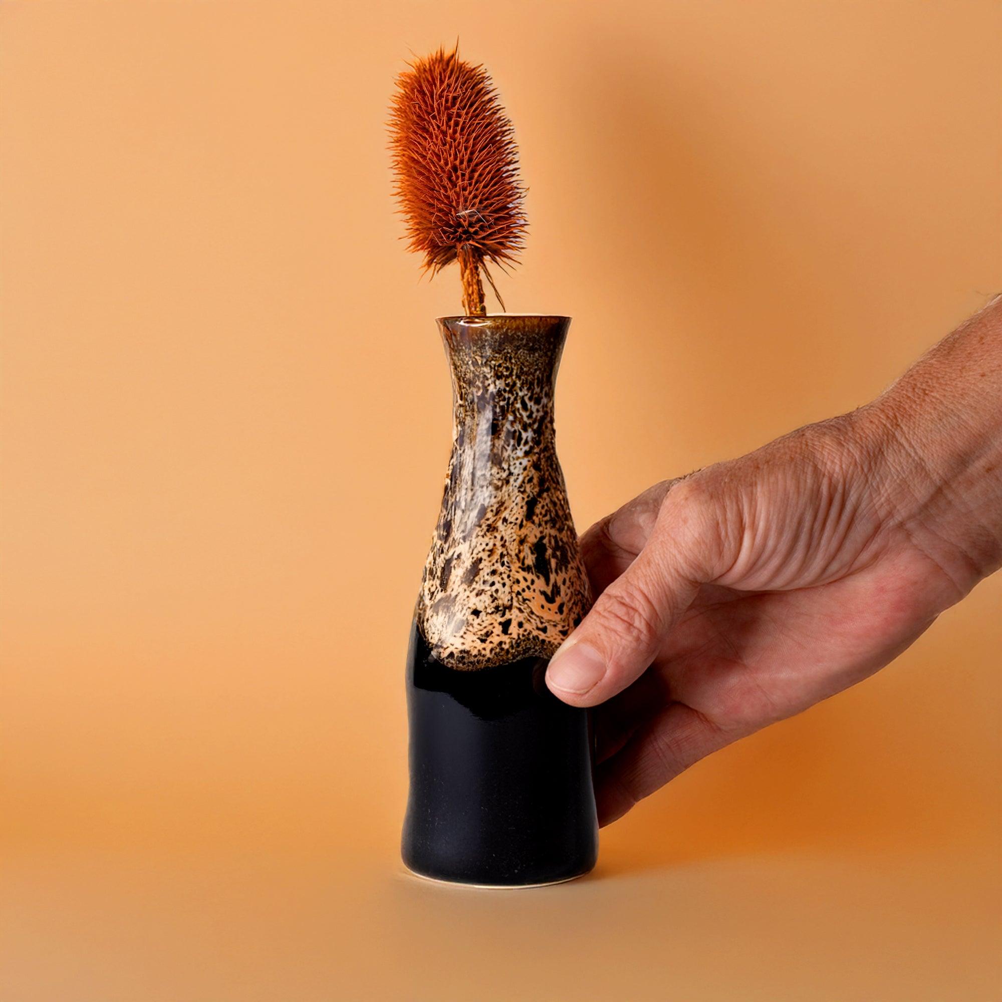 Hand holding unique ceramic flower vase with black and brown speckled design from Pottery For The Planet