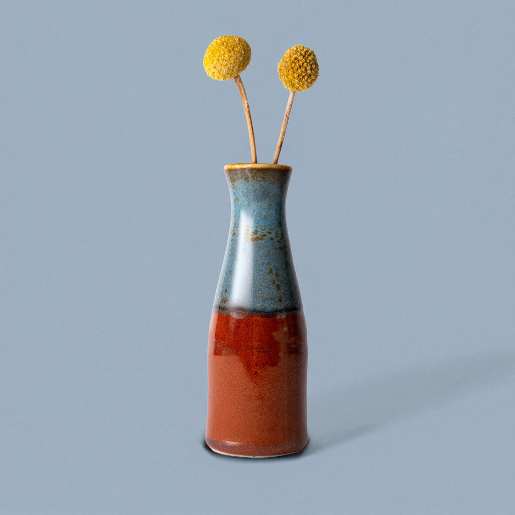 Unique ceramic flower vase by Pottery For The Planet with blue and rust glaze holding yellow billy ball flowers