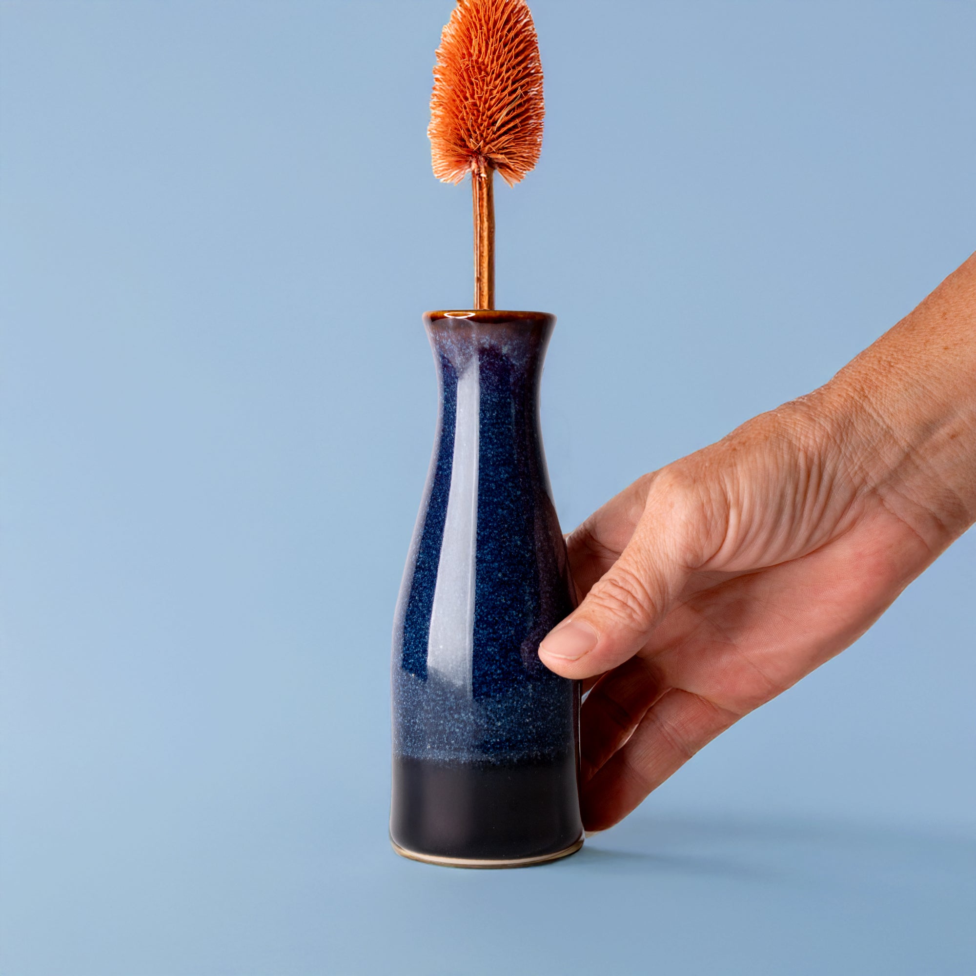 Pottery For The Planet unique ceramic flower vase in blue held by hand with orange dried flower
