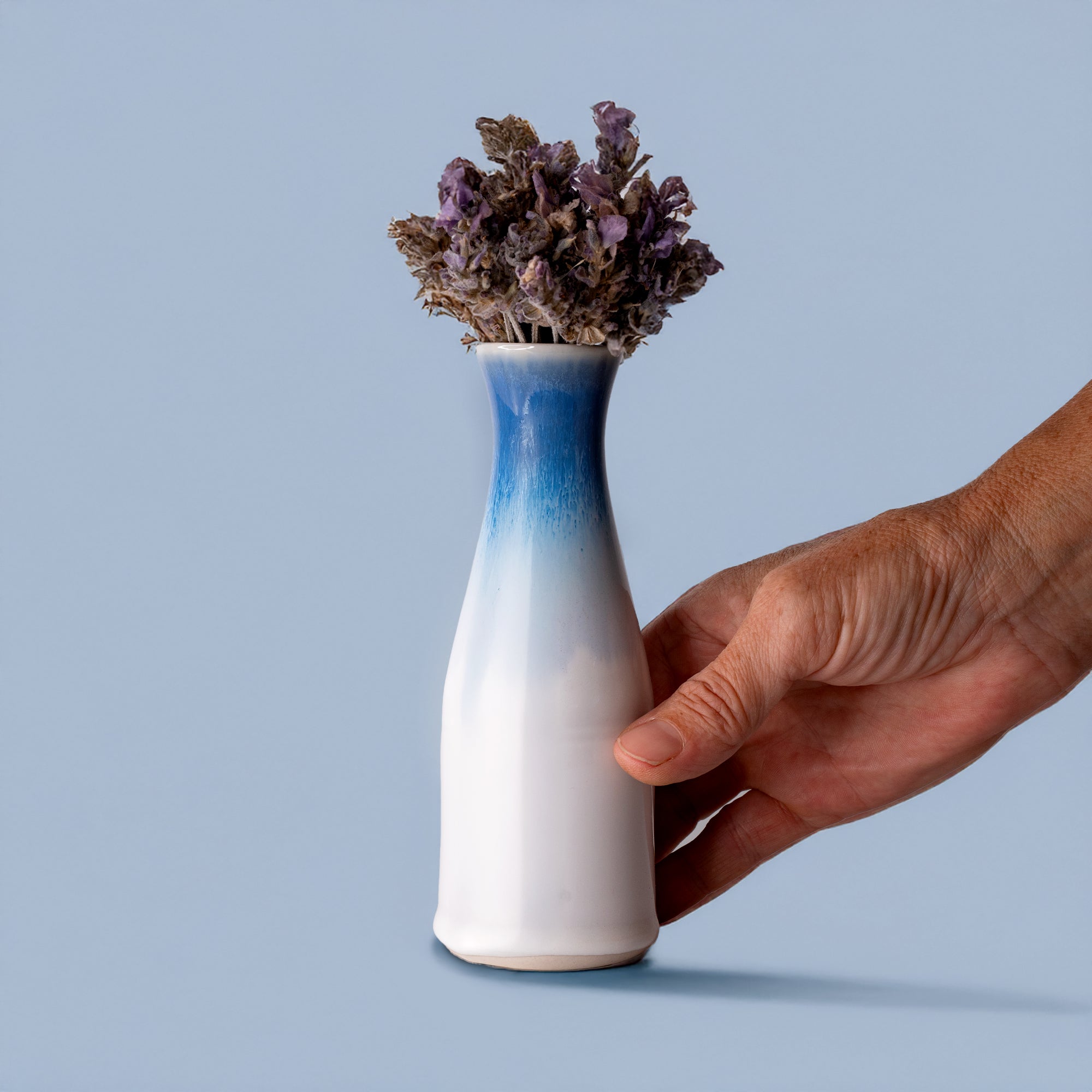 Hand holding unique ceramic flower vase with blue gradient and dried purple flowers by Pottery For The Planet