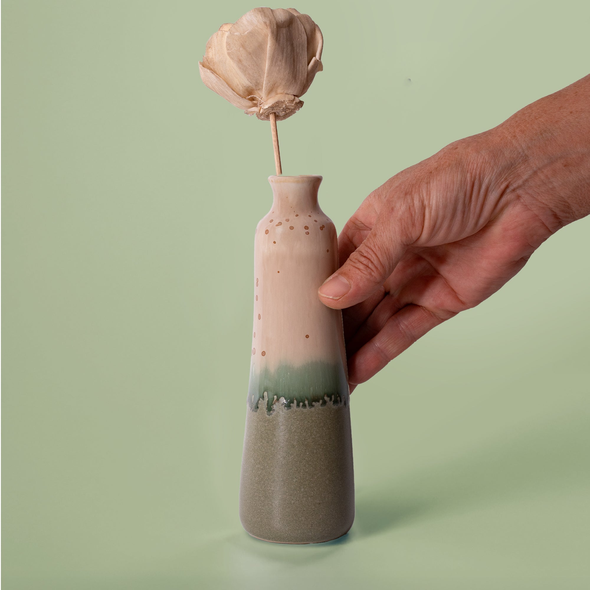 Unique handmade ceramic vase with gradient green and beige glaze held by hand with dried flower