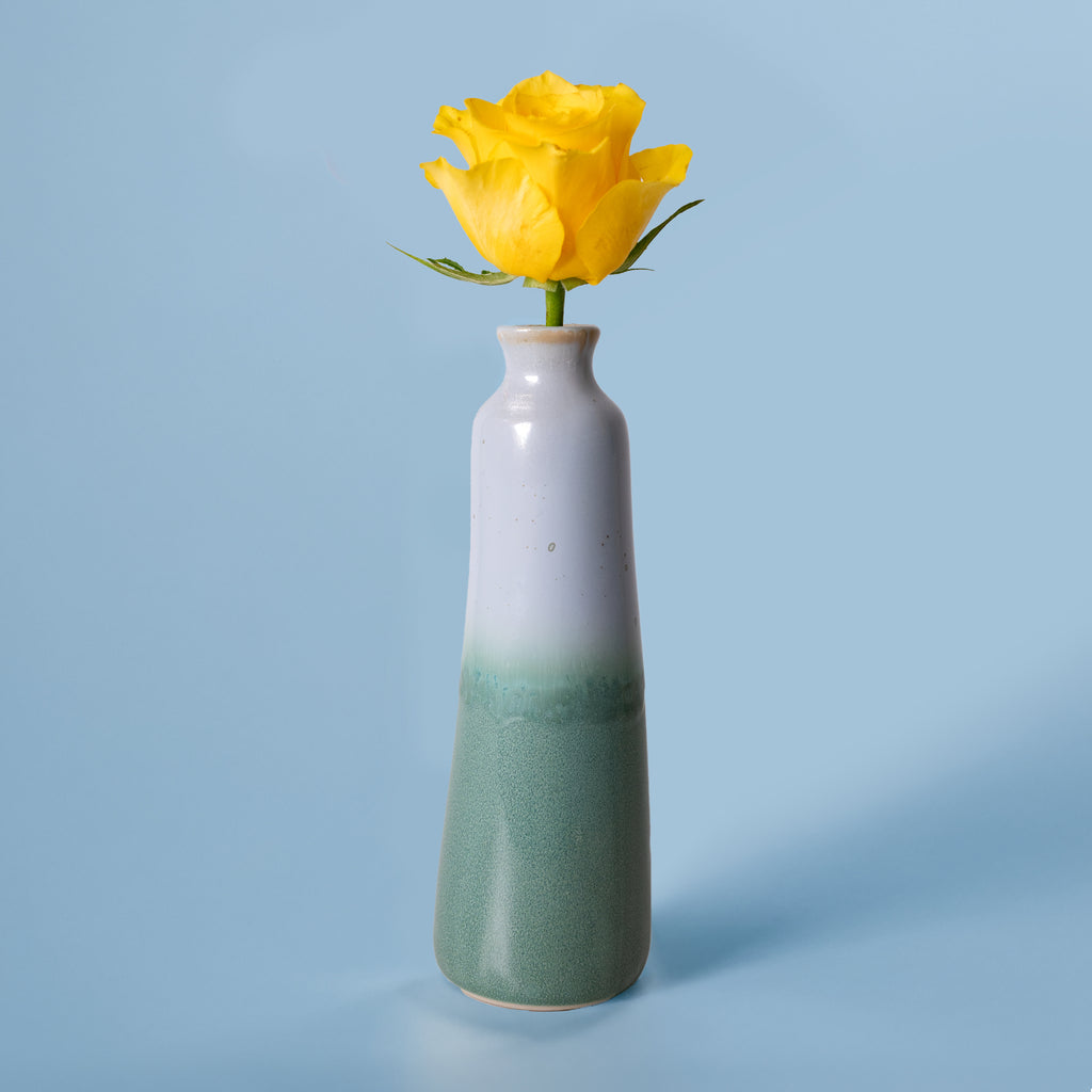Unique handmade ceramic vase with a green and white glaze holding a yellow rose on a blue background