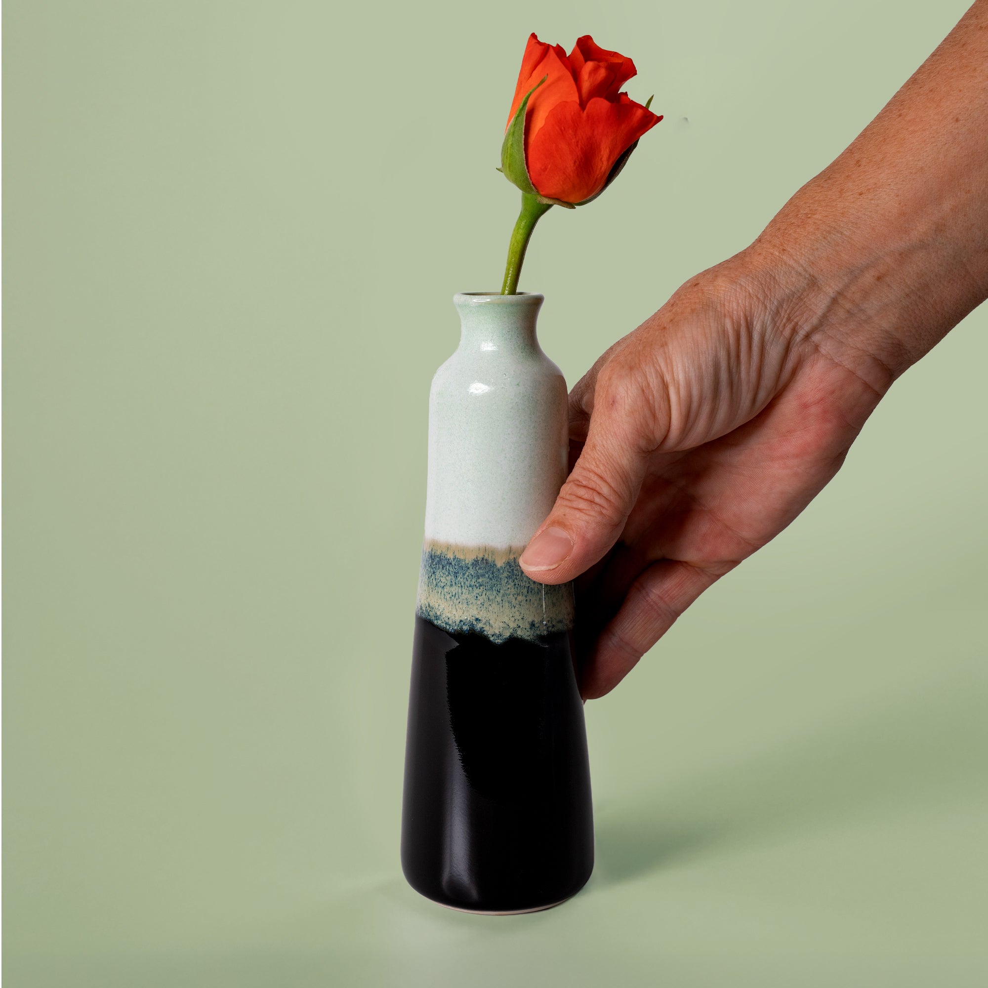 Hand holding unique handmade ceramic vase with black and white glaze containing a single red rose