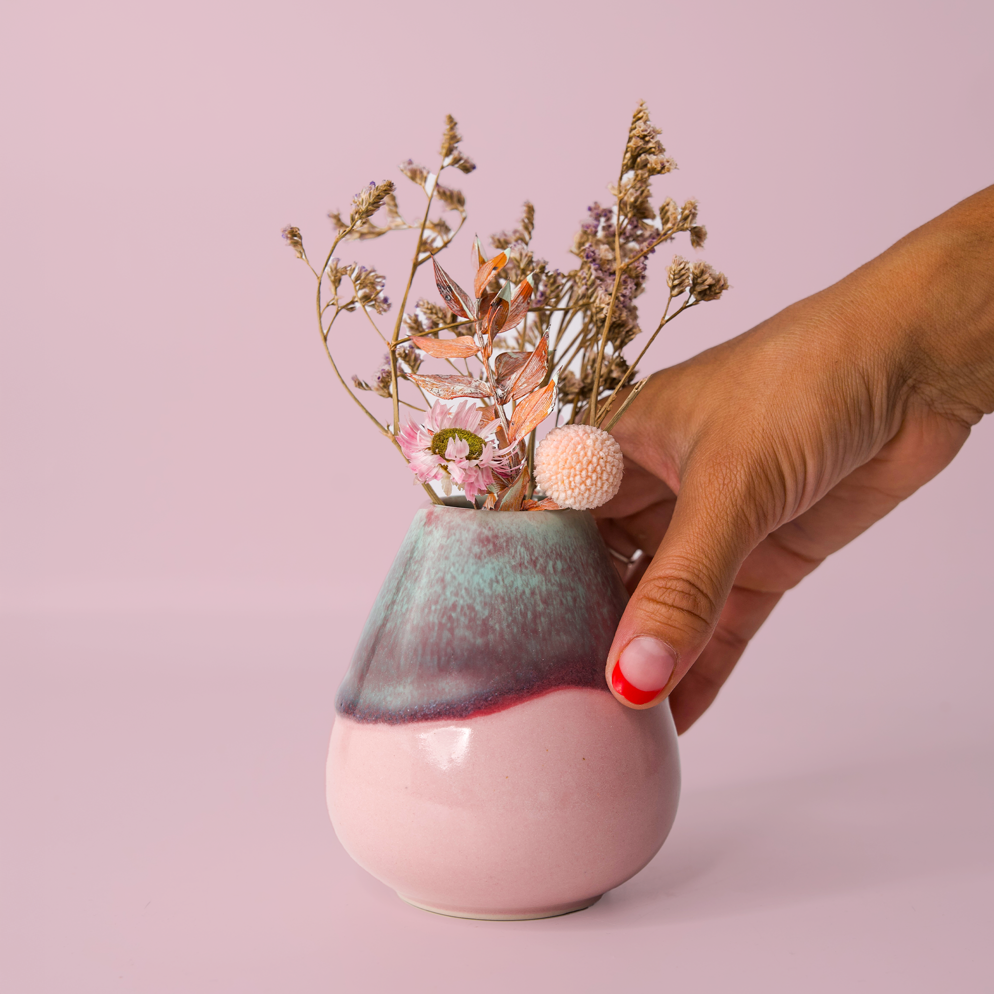Hand holding a unique pottery flower vase with pink and green glaze and dried flowers by Pottery For The Planet