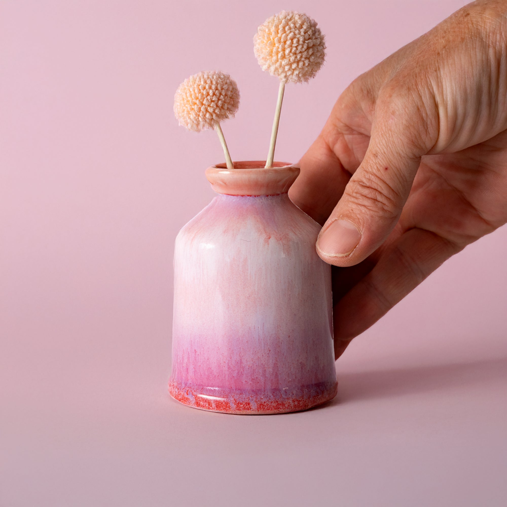 Miniature decorative vase for shelf with pink gradient glaze held by hand with dried flowers