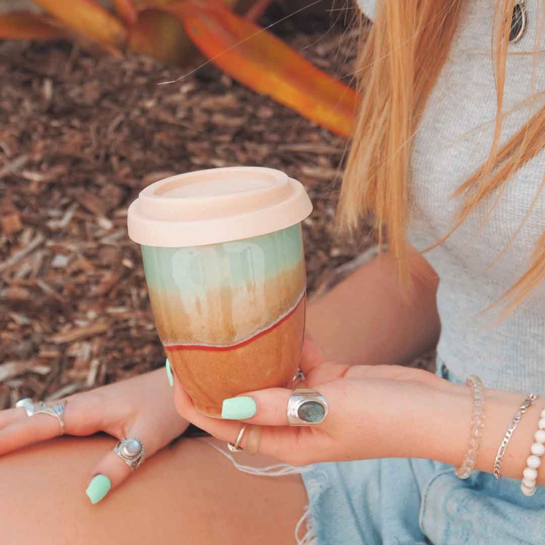 Pottery For The Planet handmade reusable cup with earthy glaze held by a person wearing bracelets and rings