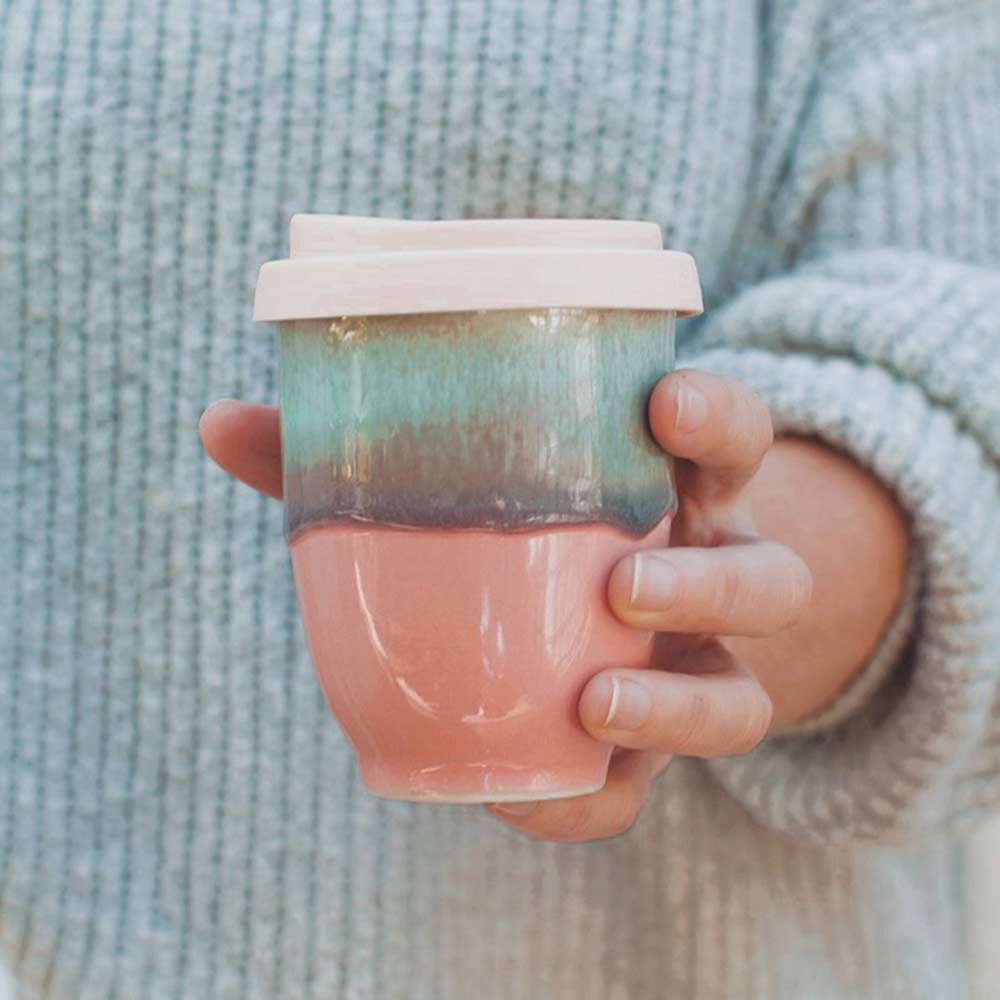 Hand holding pink ceramic travel cup with multicolor glaze and light pink lid by Pottery For The Planet